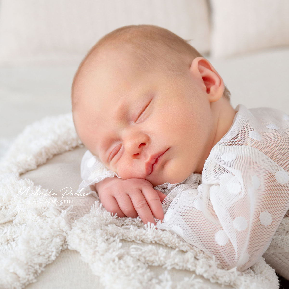 Schlafendes Neugeborenes in einem weißen, transparenten Outfit mit Punkten, liegend auf einer weichen, flauschigen Decke.